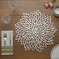 Silver vinyl floral placemat on a wooden table with utensils and glasses.