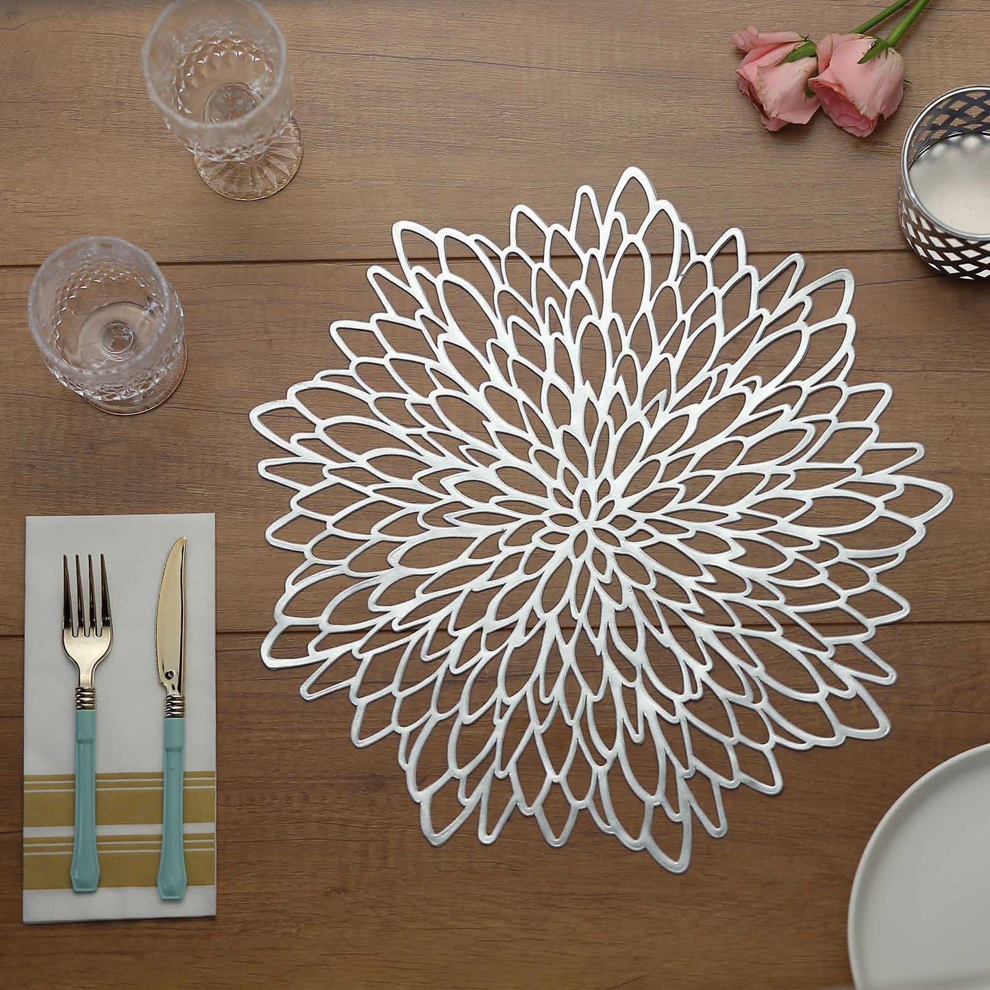 Silver vinyl floral placemat on a wooden table with utensils and glasses.