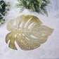 Gold monstera leaf placemat on a light gray dining table.