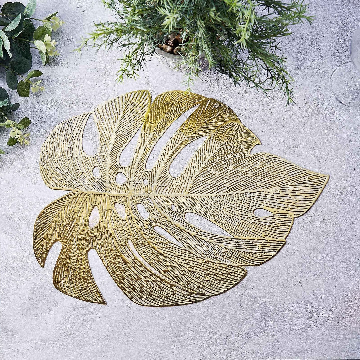 Gold monstera leaf placemat on a light gray dining table.