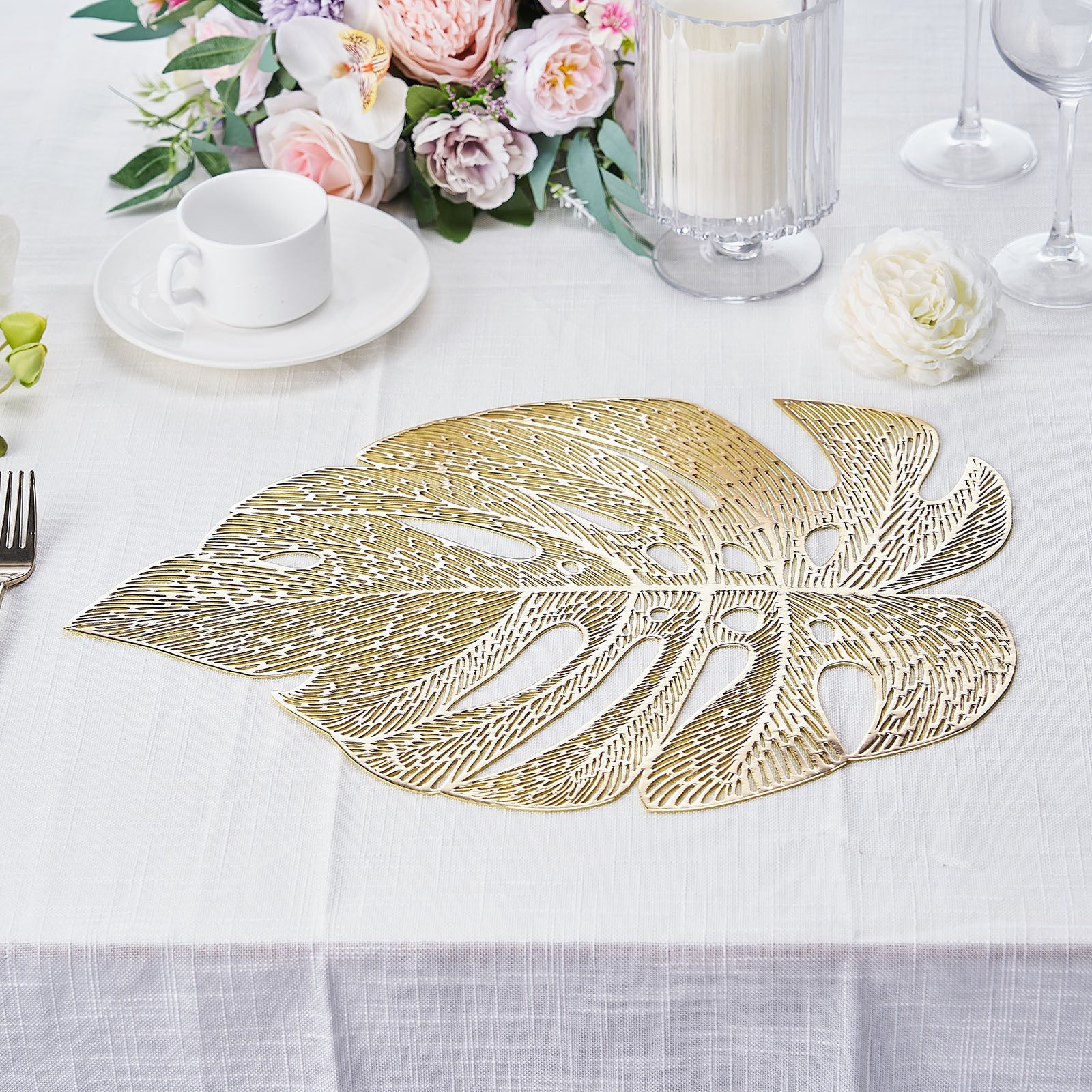 Gold monstera leaf placemat on a dining table with floral decor.