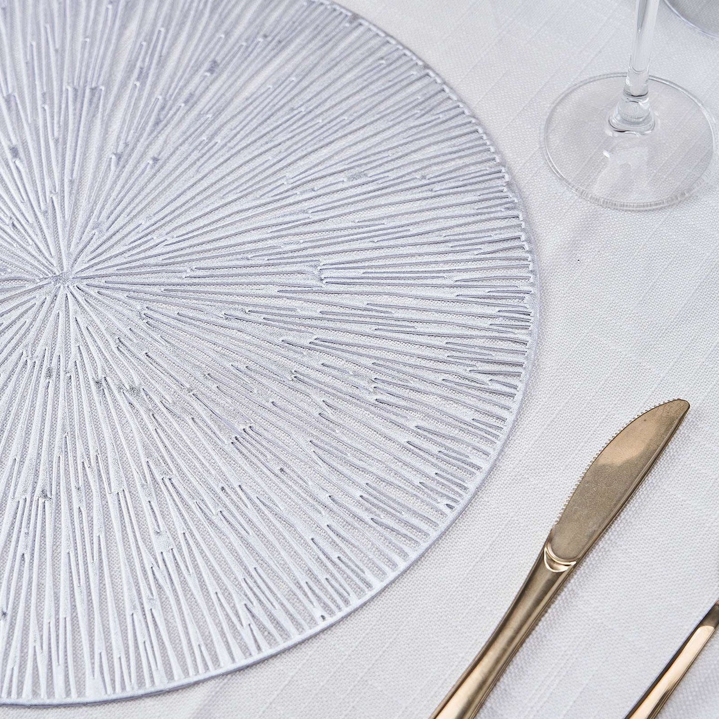 Silver metallic round placemat with a spiked design on a light table setting.
