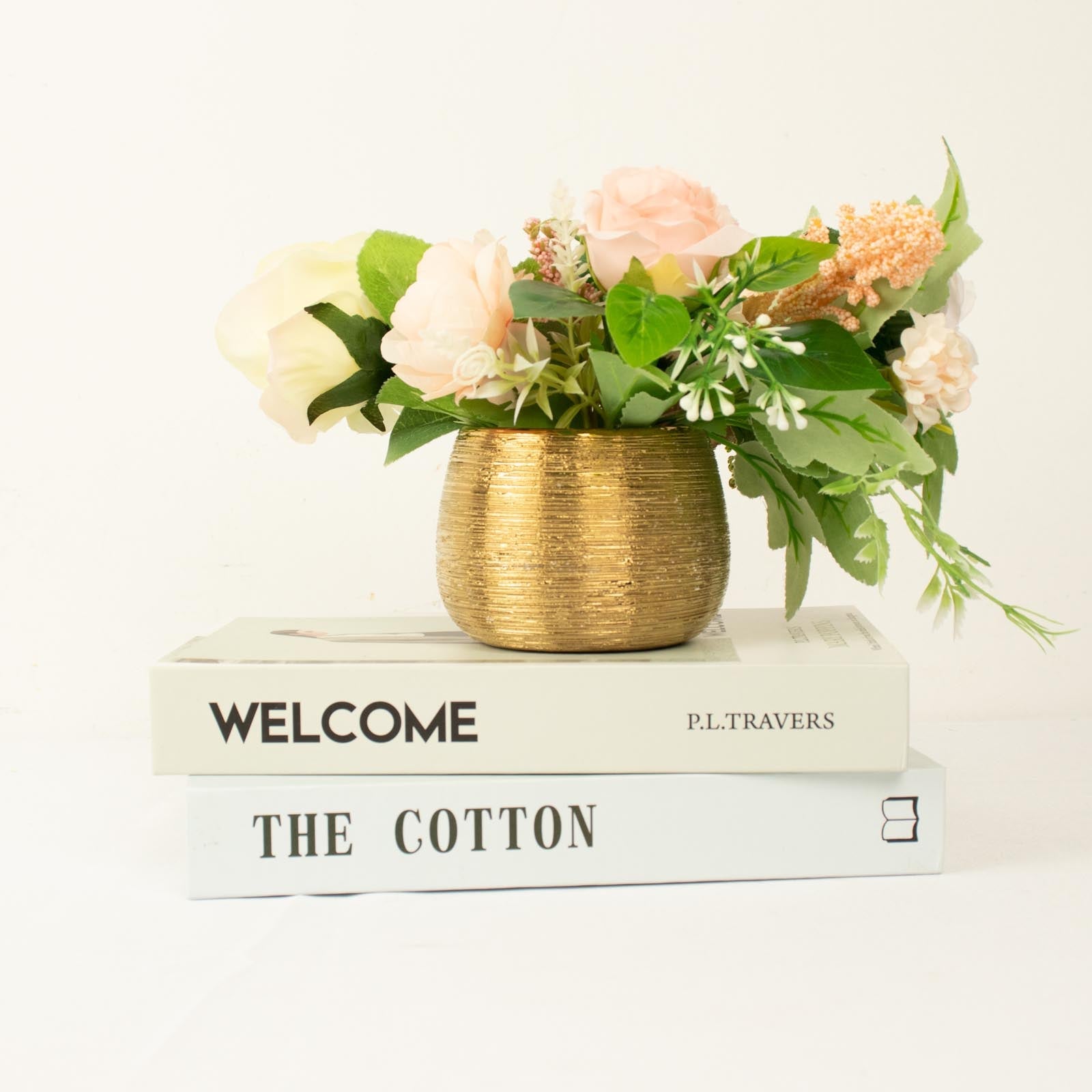 Gold textured ceramic flower vase with pastel flowers on stacked books.