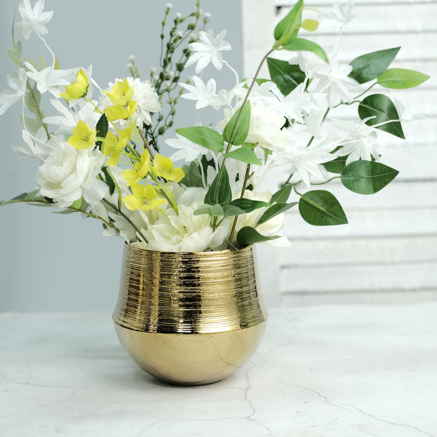 Gold textured round ceramic flower pot with white and yellow flowers.
