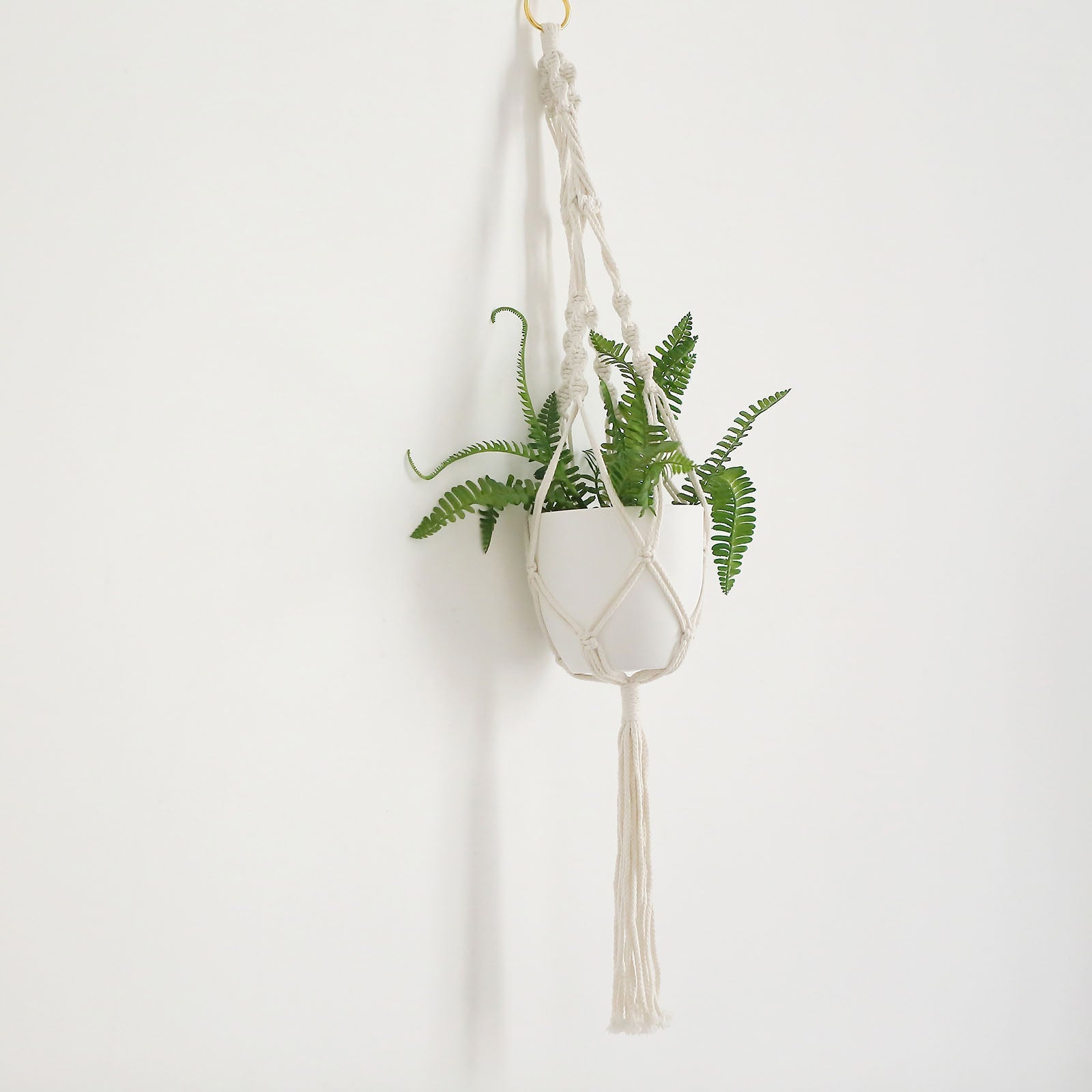 Ivory macrame hanging planter basket with tassel and greenery.