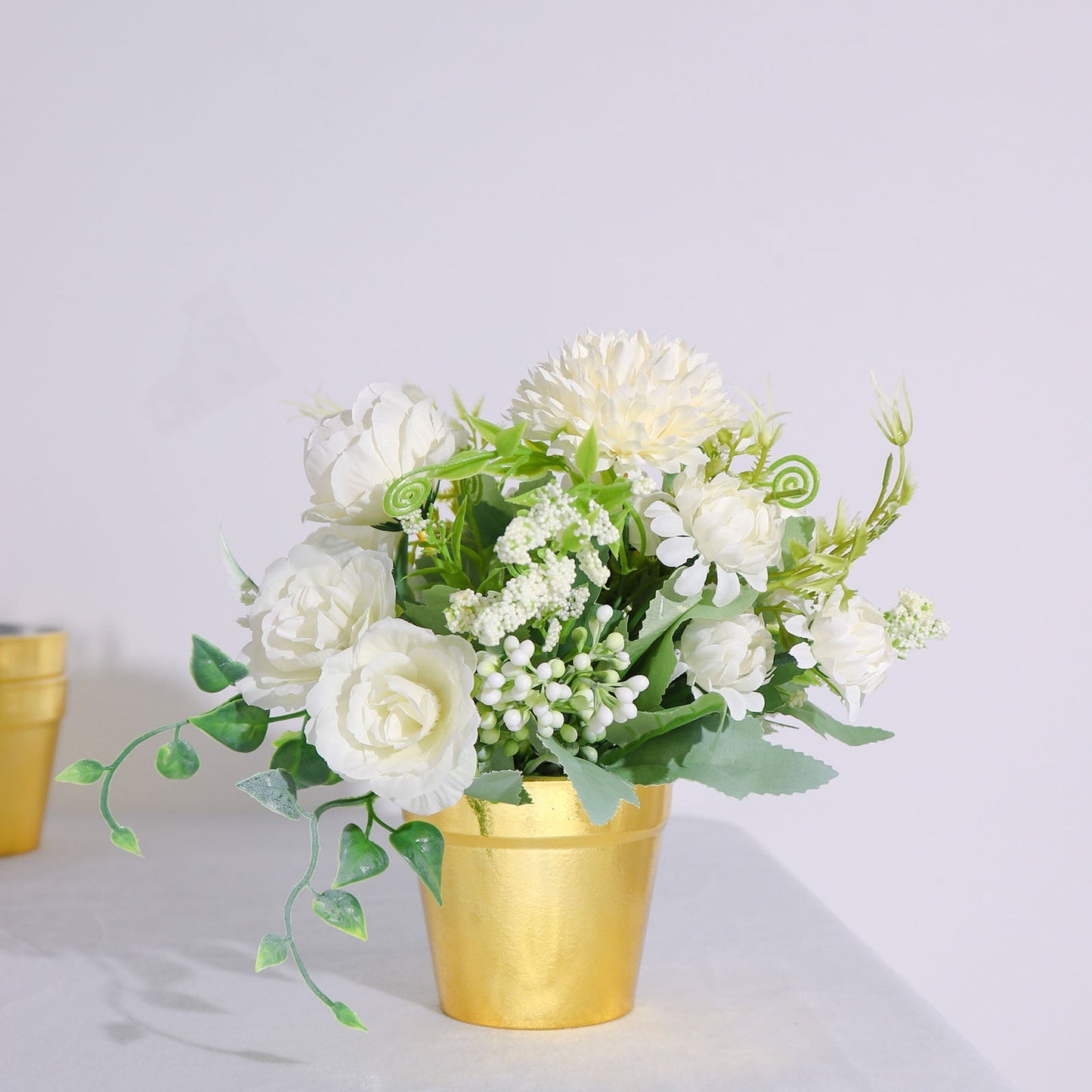 Gold plastic party favor bucket with white flowers and greenery.