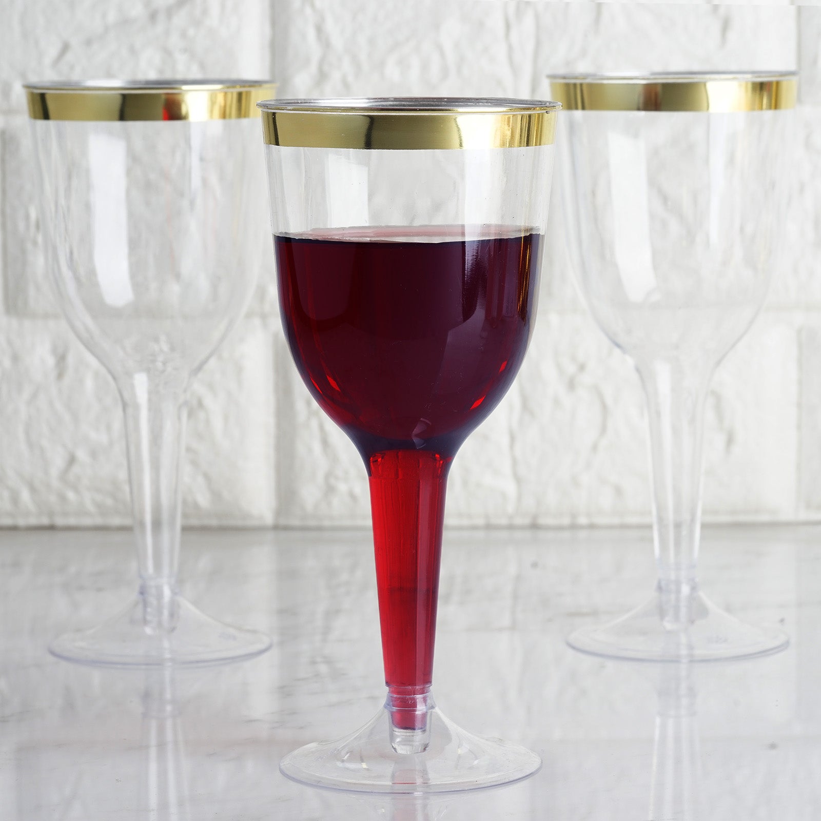 9oz clear plastic wine goblet with gold rim, filled with red beverage.