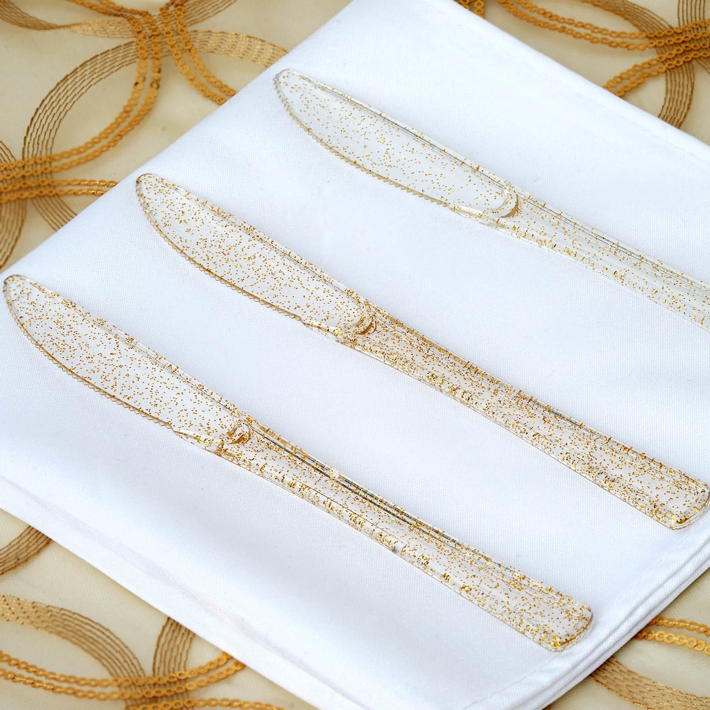 Clear gold glittered plastic knives on a white napkin.