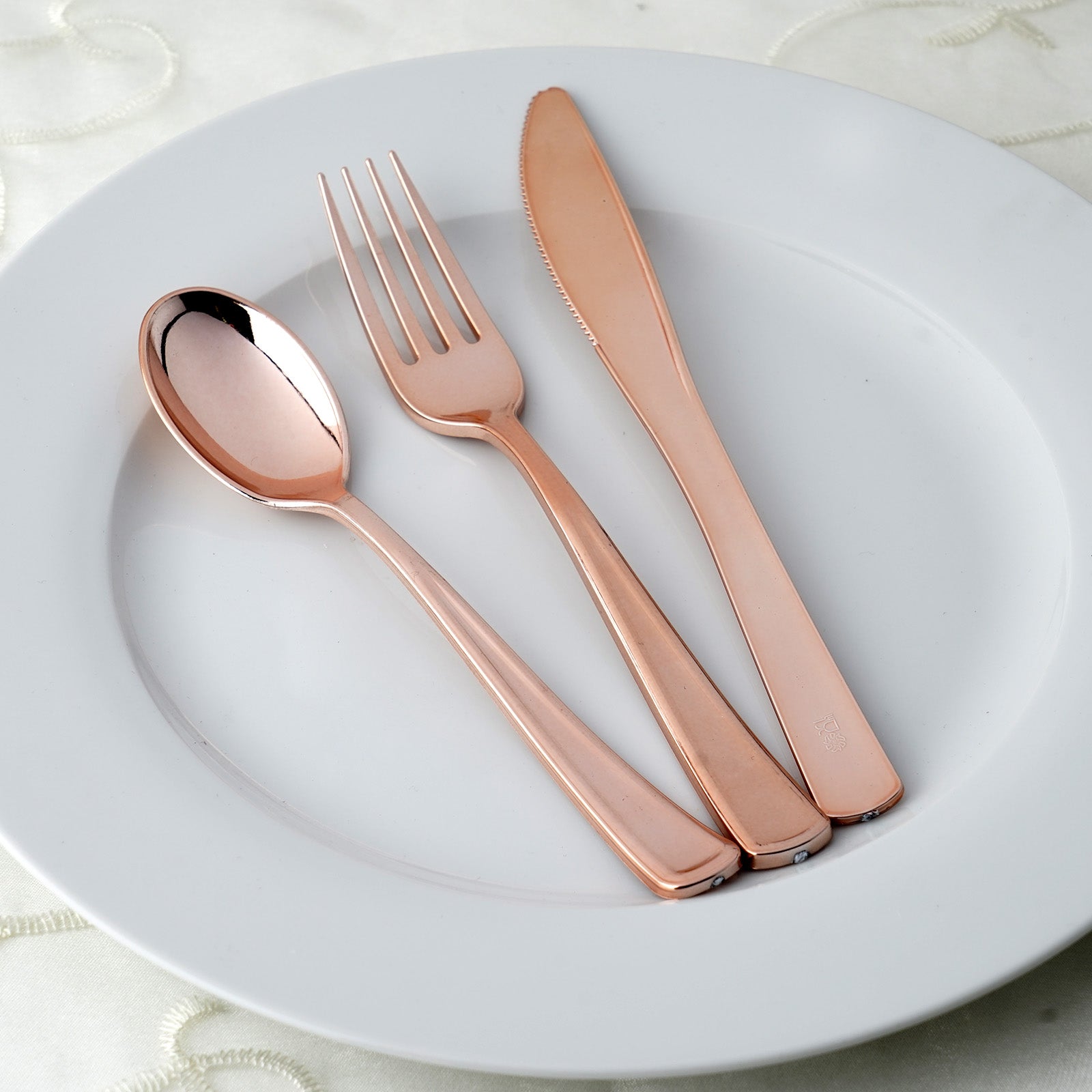 Rose gold disposable cutlery set on a white plate.