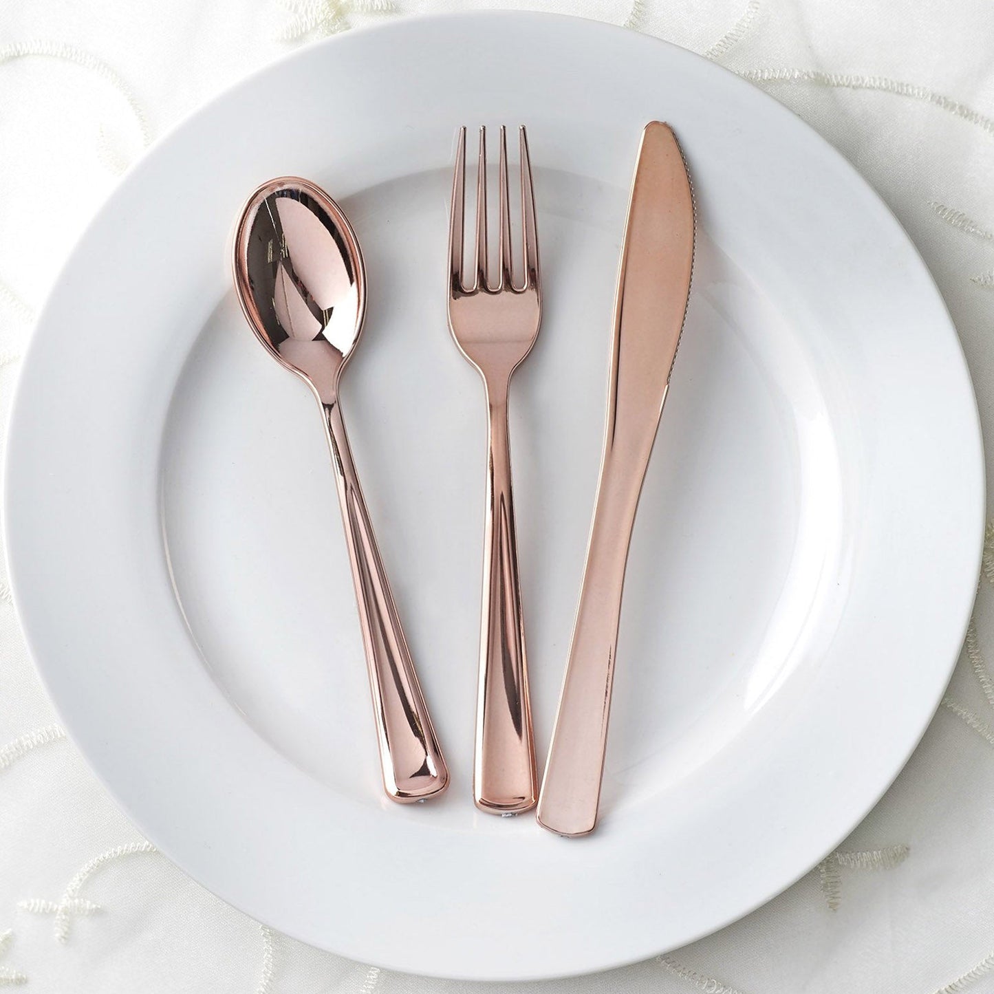 Metallic rose gold disposable cutlery set on a white plate.