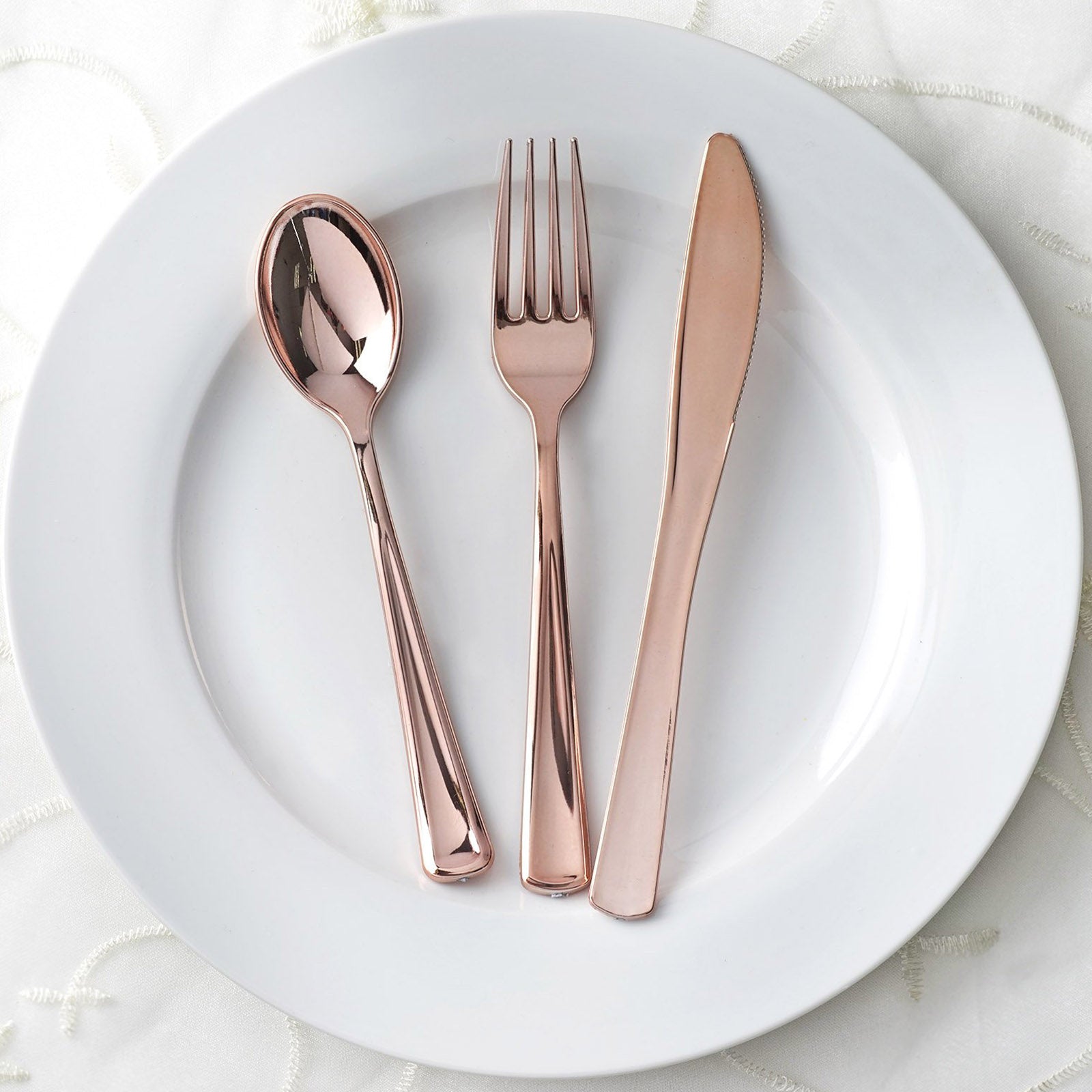 Metallic rose gold disposable cutlery set on a white plate.