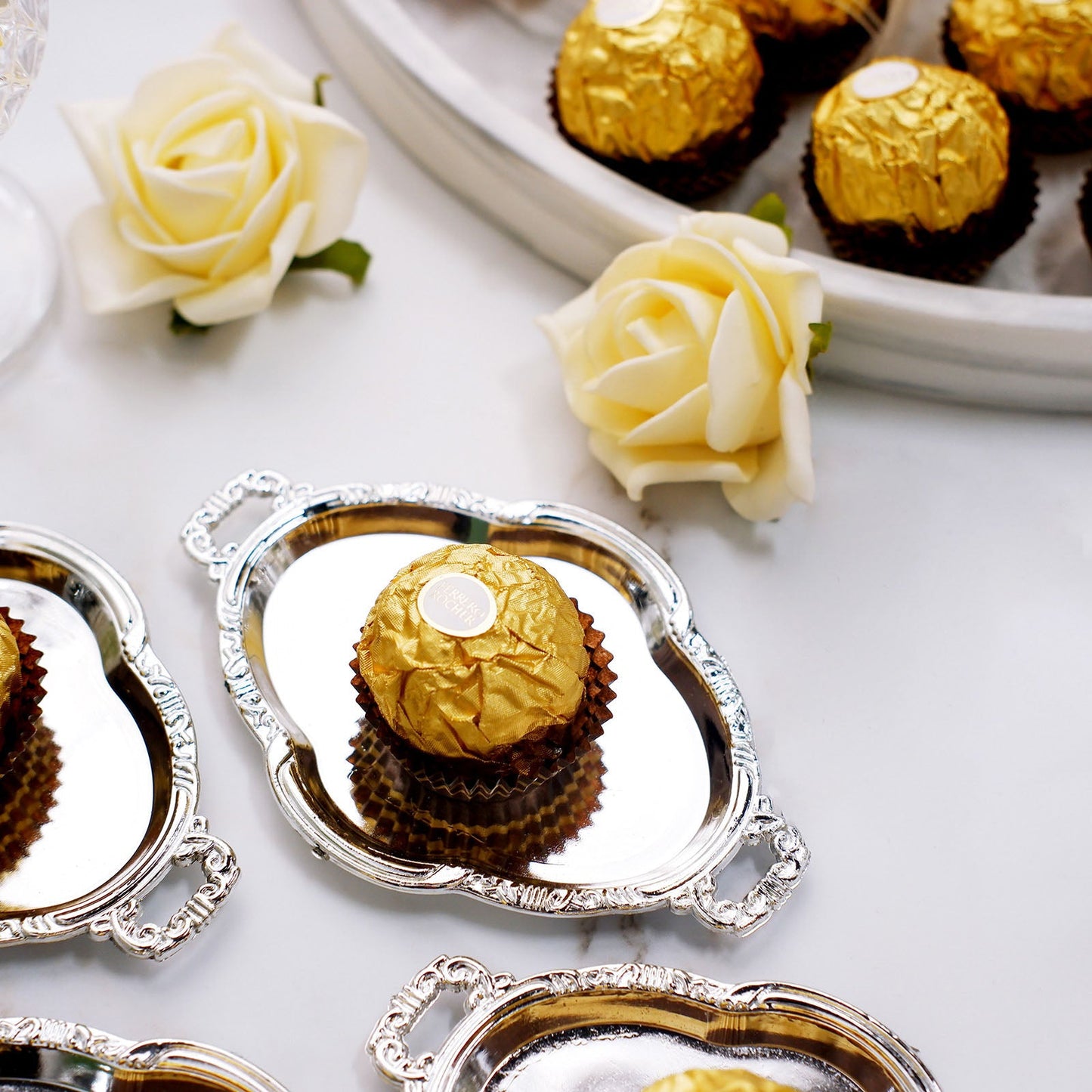 Silver oval mini party favor tray with chocolate treat and decorative flowers.