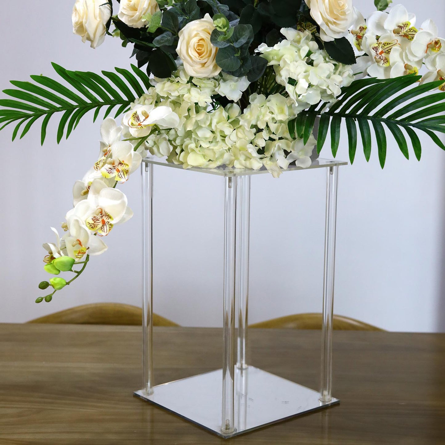 Clear acrylic wedding centerpiece vase with flowers and greenery.