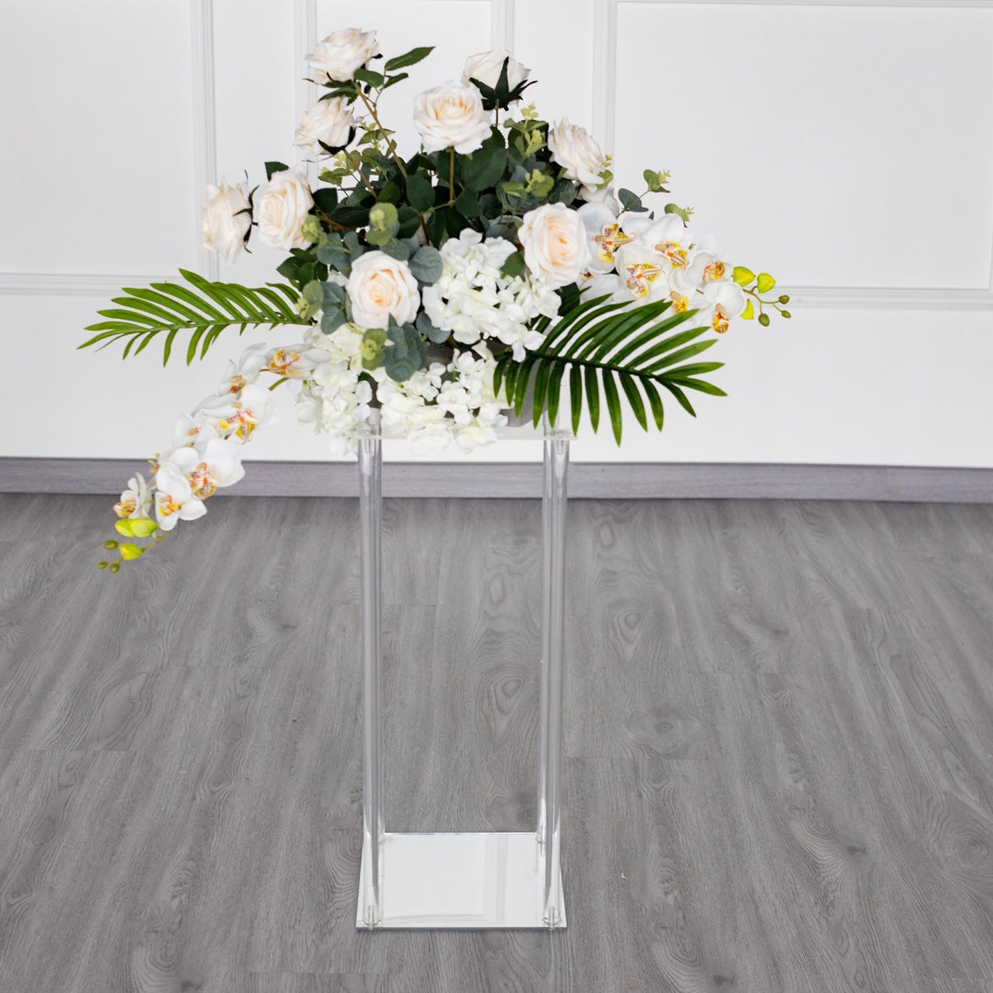 Clear acrylic wedding centerpiece vase with flowers on a square mirror base.
