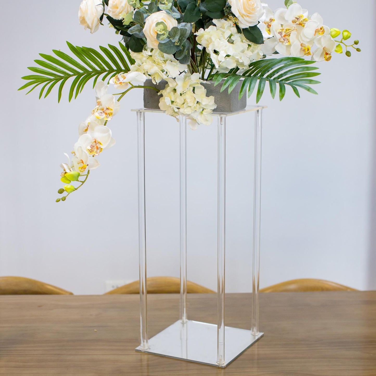 Clear acrylic wedding centerpiece vase with flowers and square mirror base.