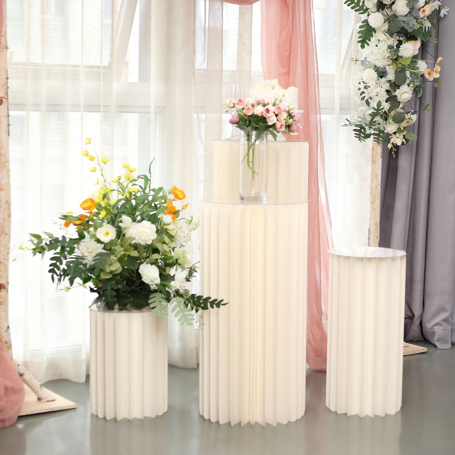 Ivory cylinder display column stand with flowers on top.