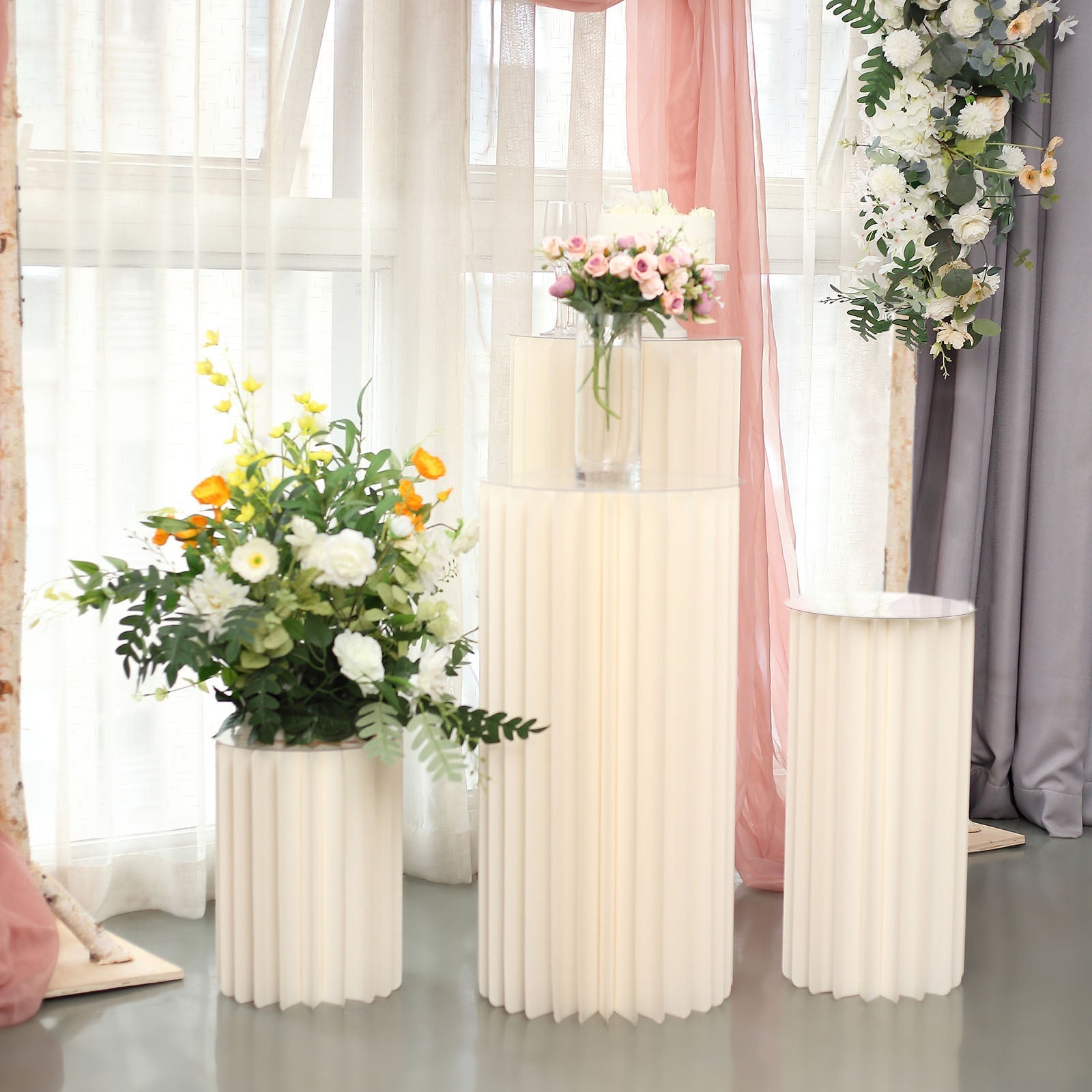 Ivory cylinder display column stand with flowers on top.