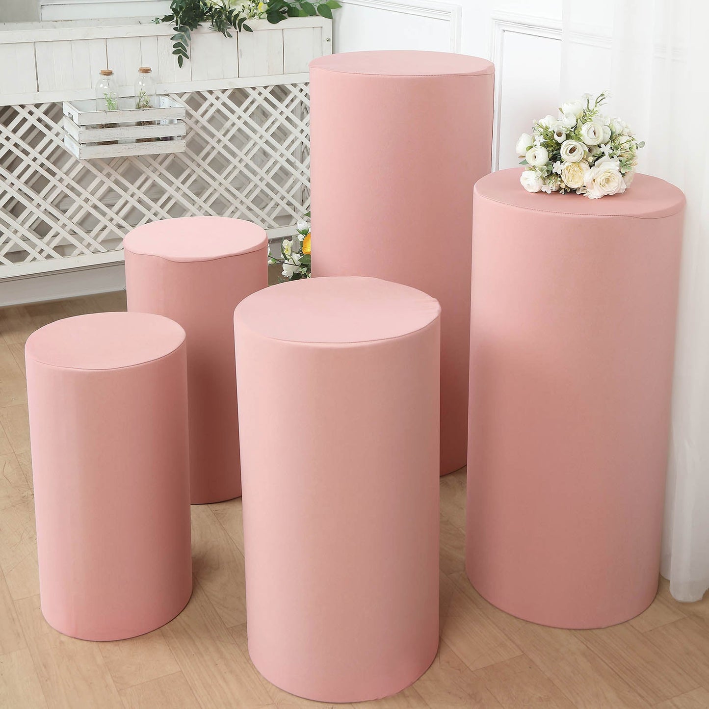 Dusty rose spandex pedestal stand covers arranged with flowers on top.