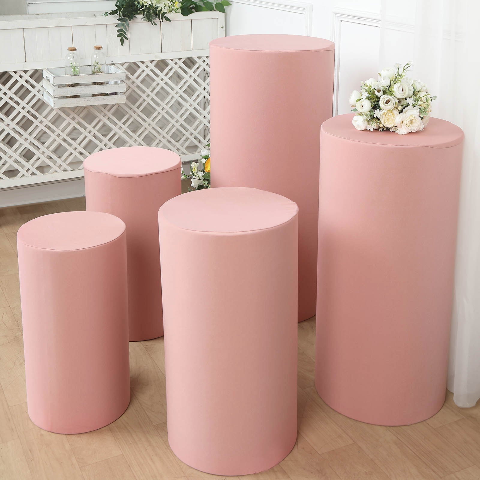 Dusty rose spandex pedestal stand covers arranged with flowers on top.