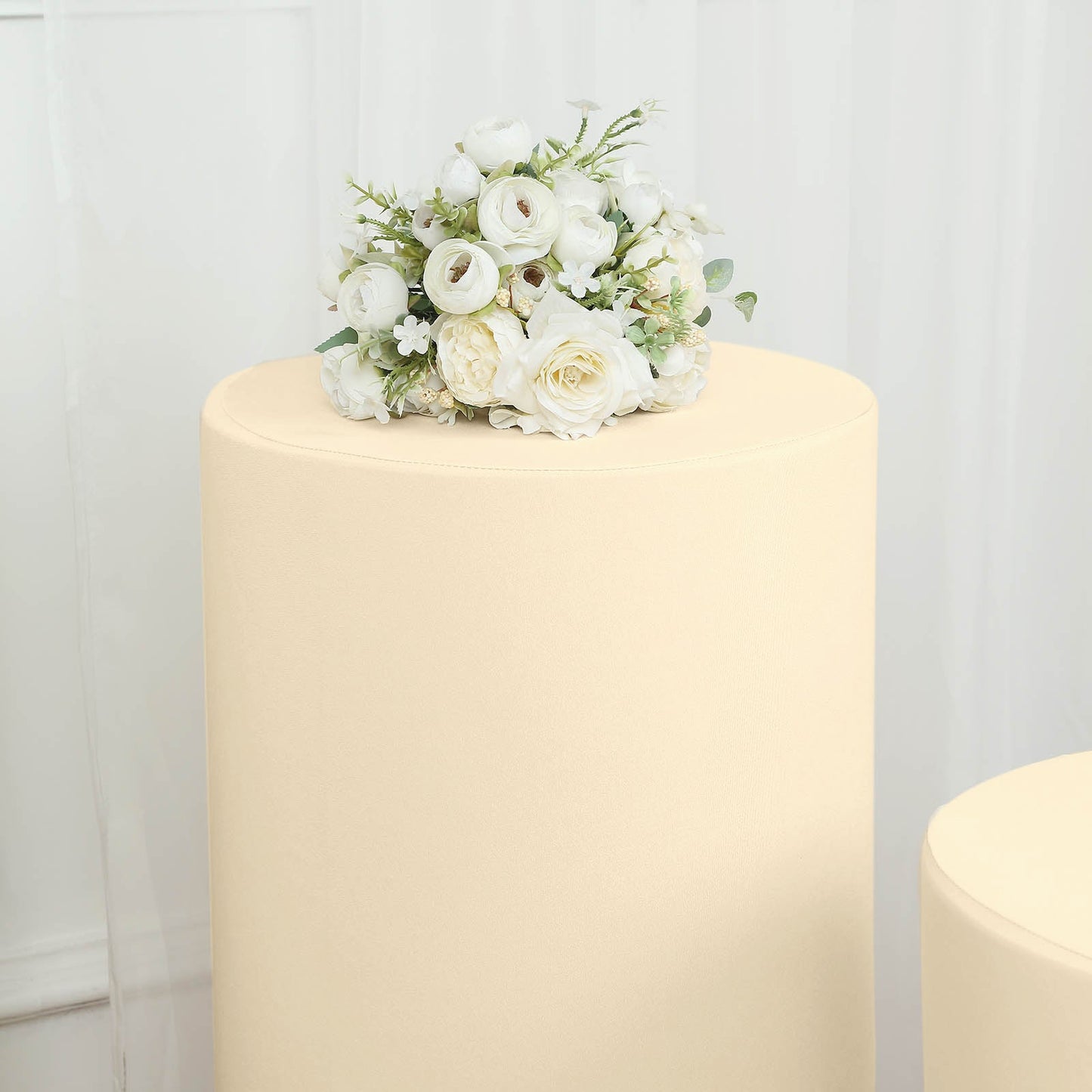 Beige spandex pedestal stand cover with decorative white flowers.