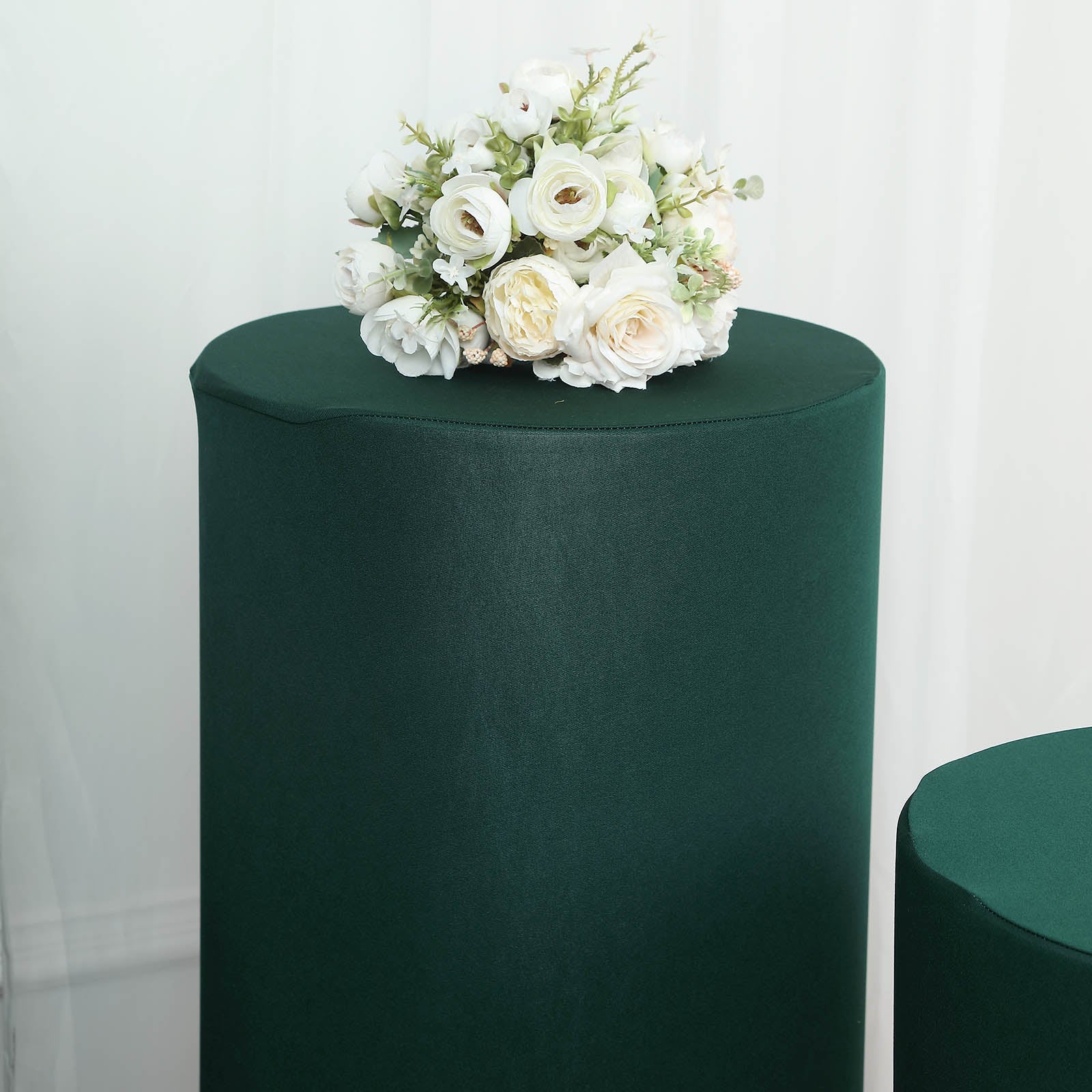 Emerald green spandex pedestal stand covers with a floral arrangement on top.