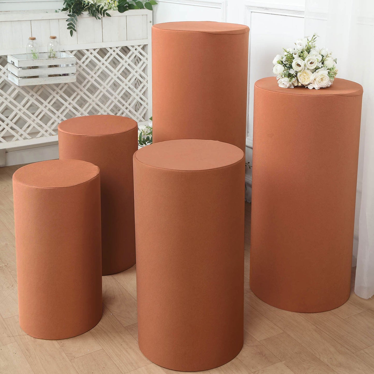 Set of 5 rust spandex cylinder pedestal stand covers for events.