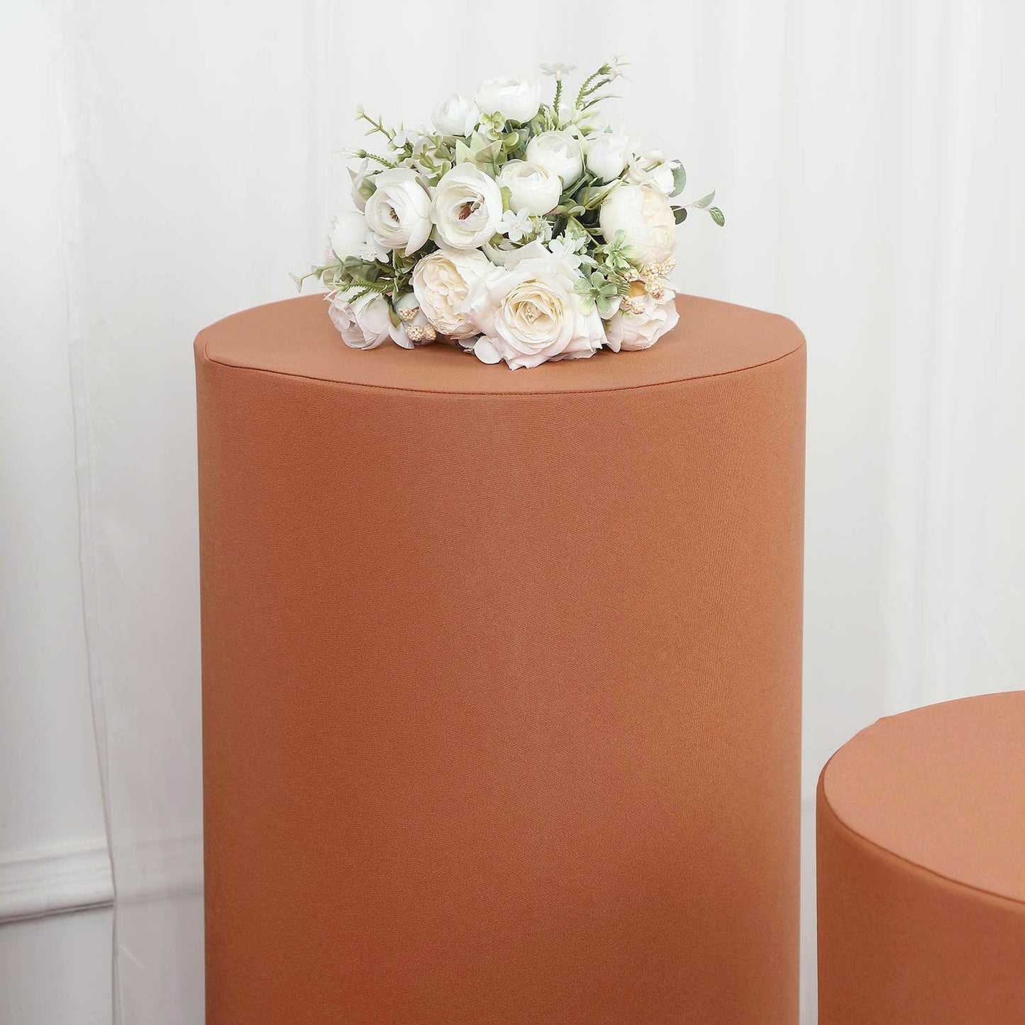 Rust spandex cylinder pedestal stand cover with flowers on top.