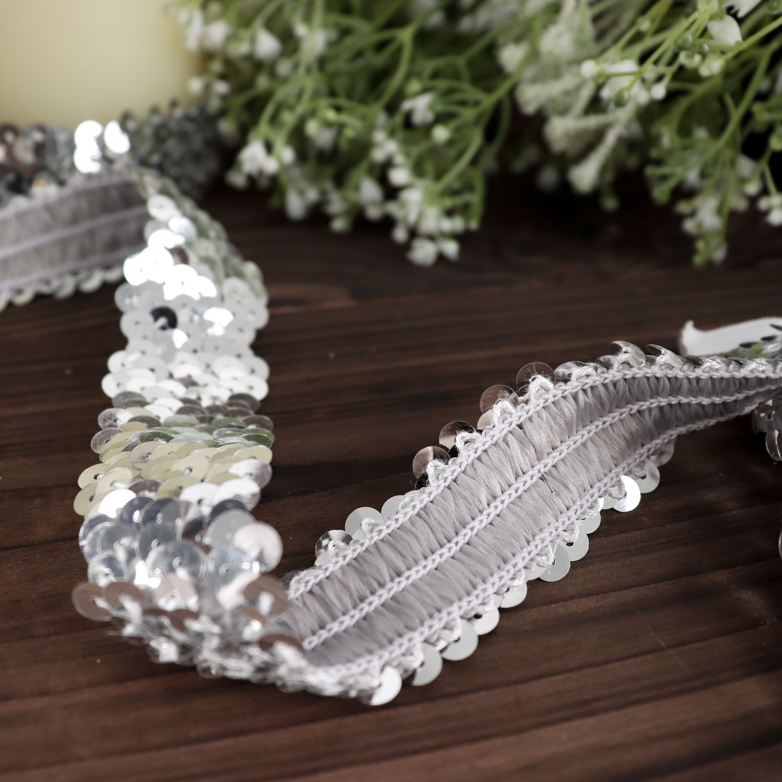 Metallic silver sequin stretch fabric ribbon on a wooden surface.