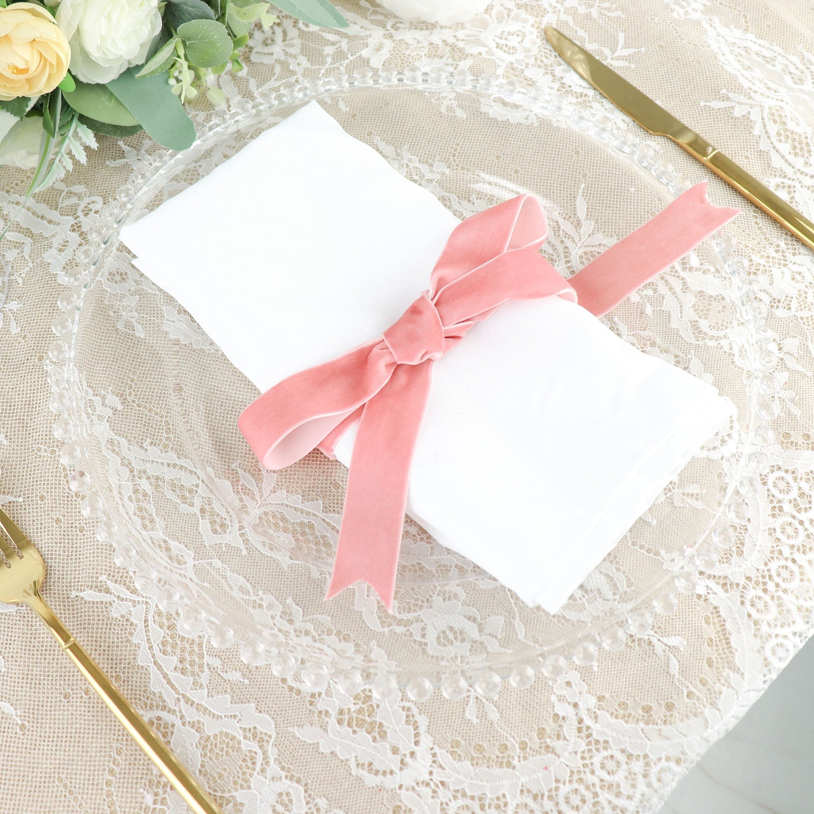 Dusty rose velvet ribbon tied around a napkin on a decorative plate.