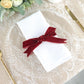 Burgundy velvet ribbon tied around a white napkin on a lace table setting.