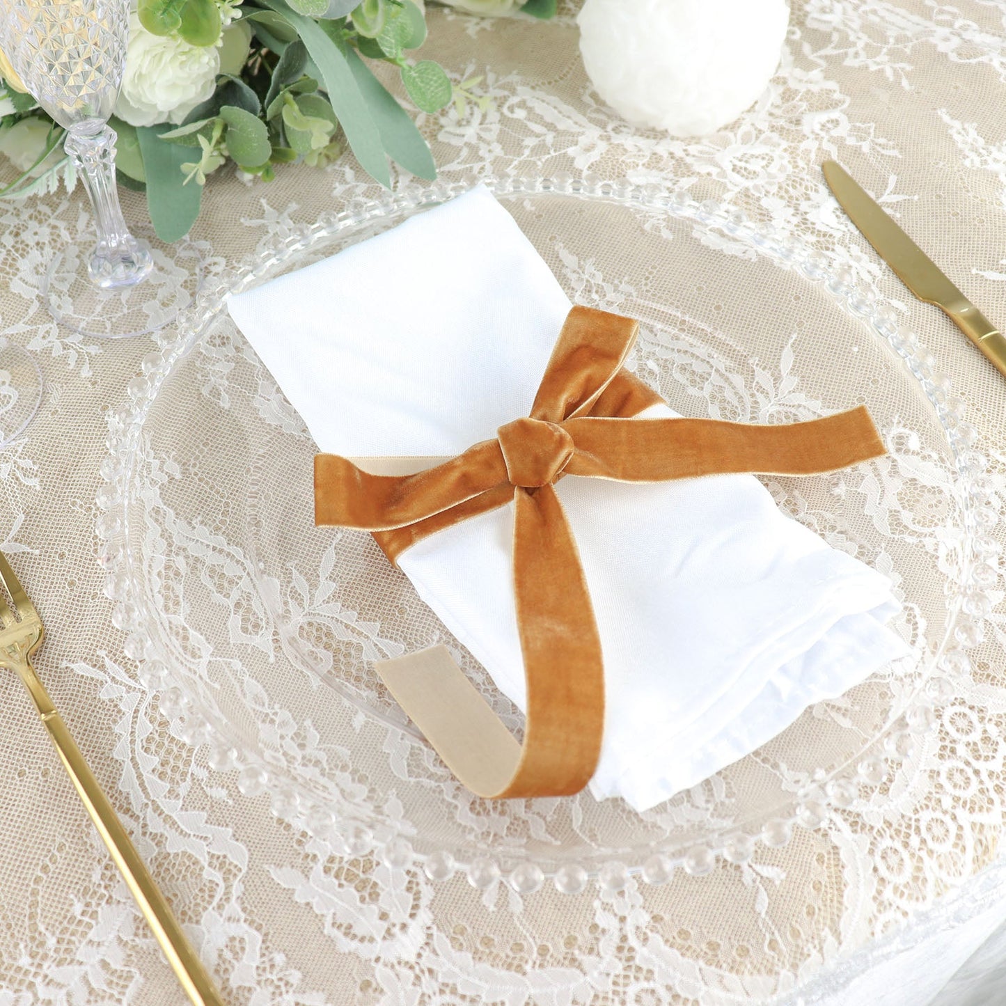 Gold velvet ribbon tied around a white napkin on a decorative plate.