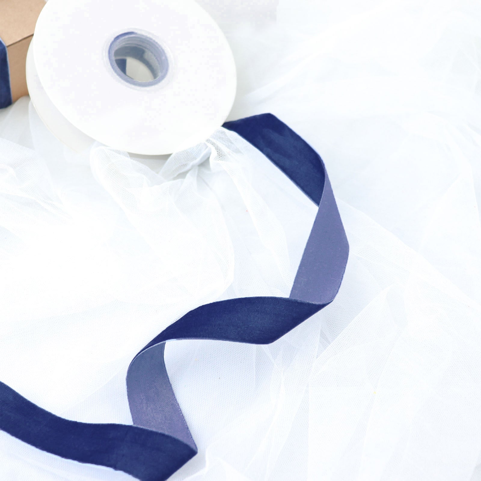 Navy blue velvet ribbon spool on white tulle fabric.