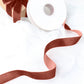 Terracotta velvet ribbon spool on a white fabric background.