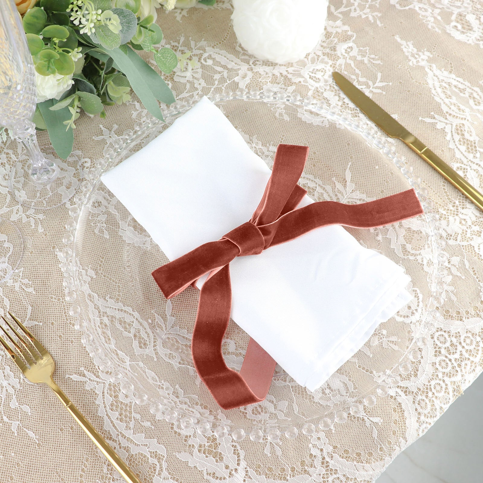 Terracotta velvet ribbon spool tied around a napkin on a dining table setting.