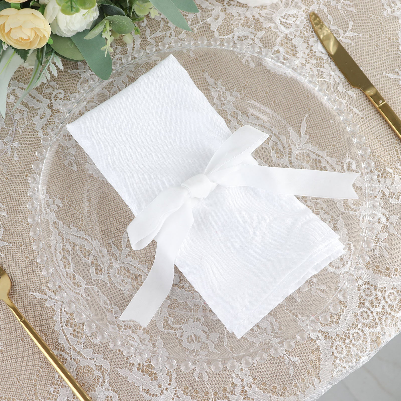 White velvet ribbon tied around a napkin on a decorative plate.