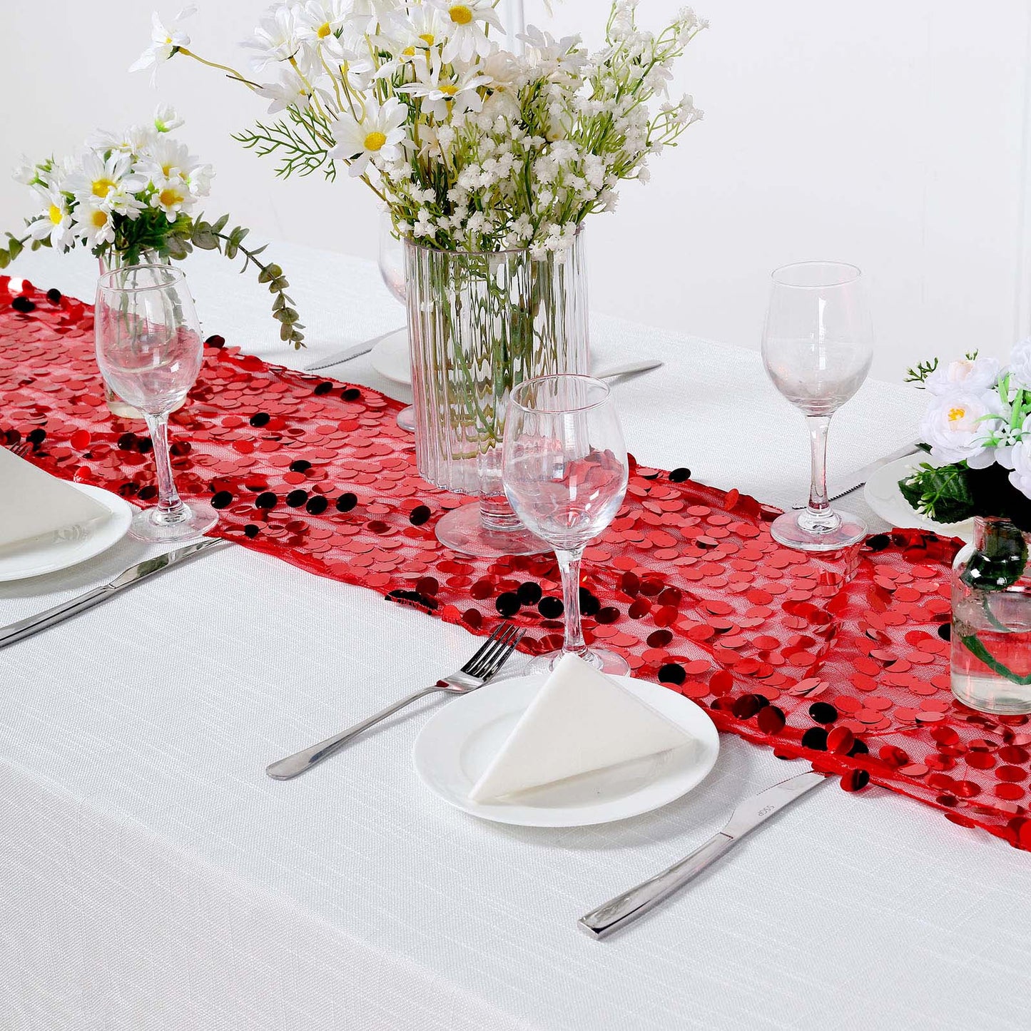 Red sequin table runner on a dining table with flowers and dinnerware.