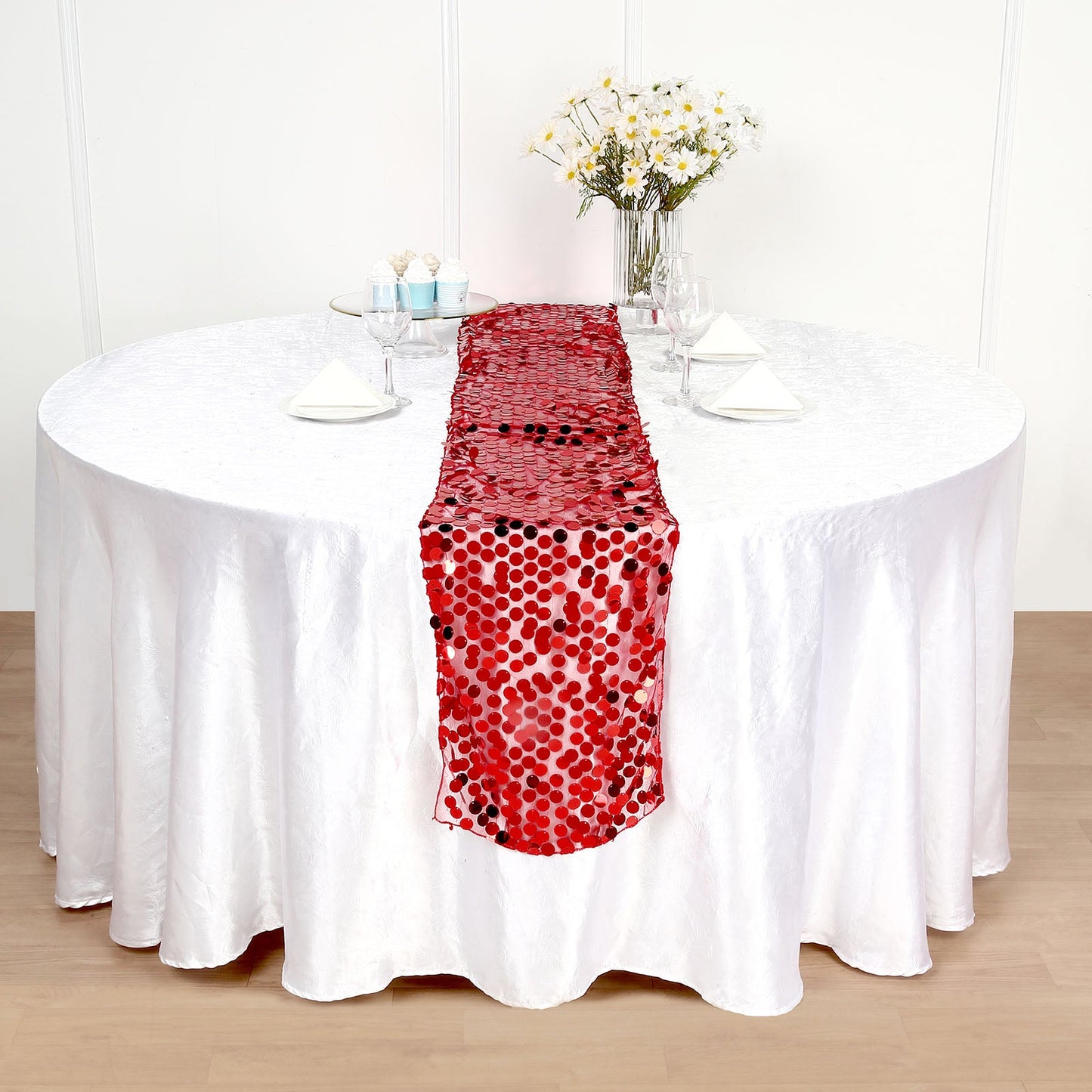 Red sequin table runner on a round table with white tablecloth.