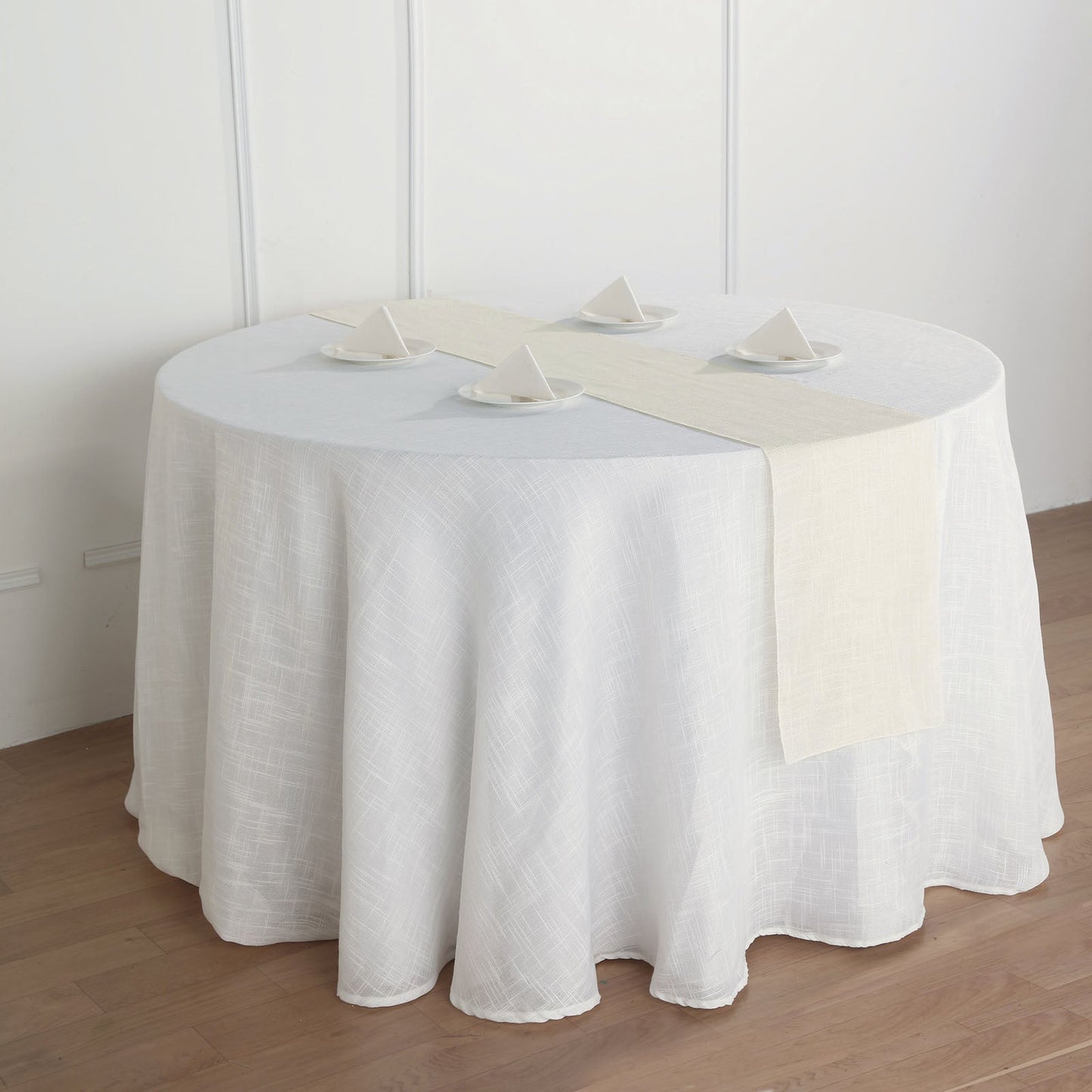 Ivory linen table runner on a round table with decorative plates.