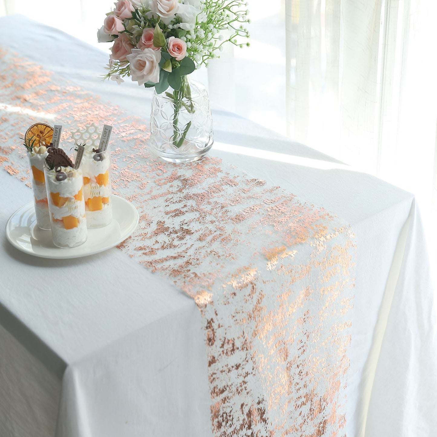 Metallic rose gold foil thin mesh polyester disposable table runner on a white table.