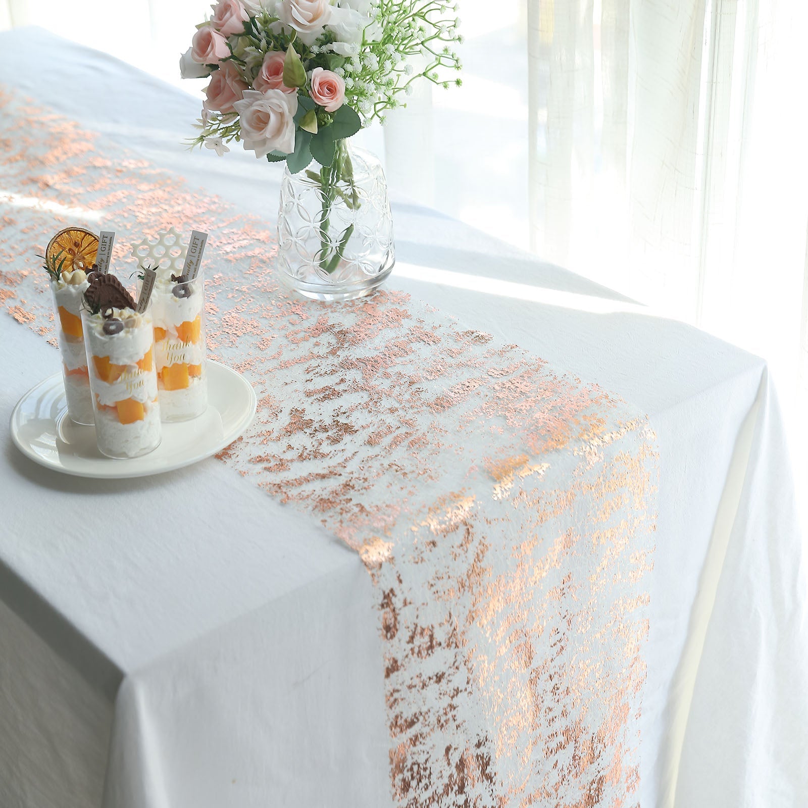 Metallic rose gold foil thin mesh polyester disposable table runner on a white table.