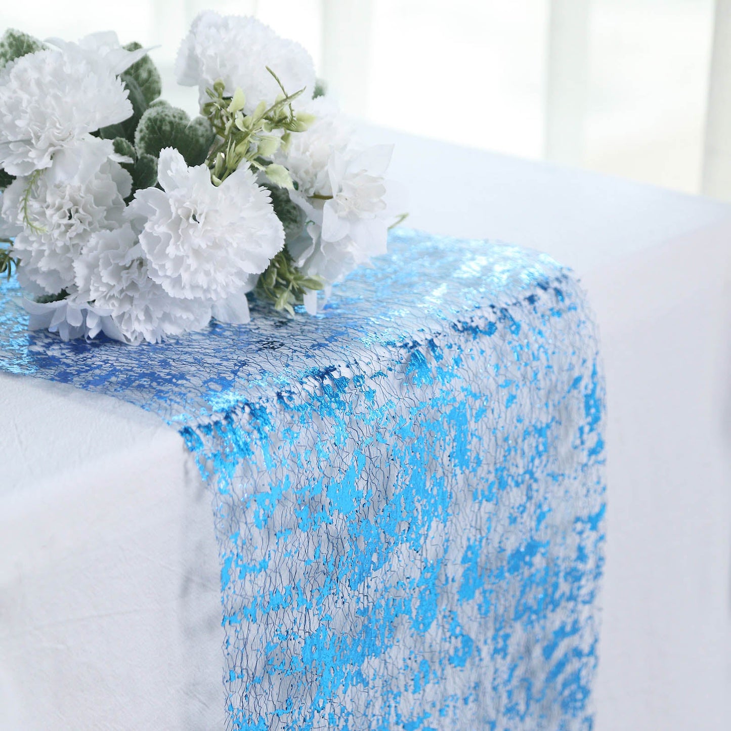 Sparkly metallic royal blue foil table runner on a white table with flowers.
