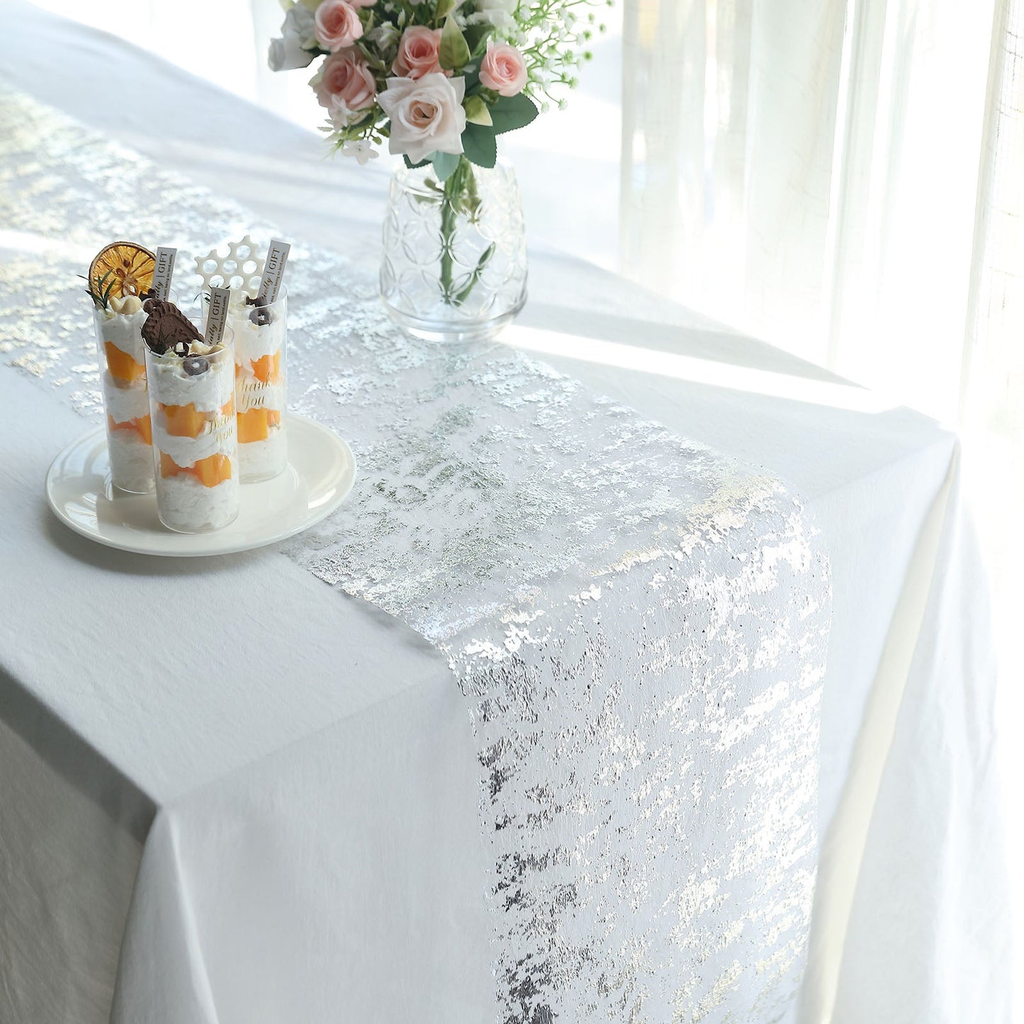 Sparkly metallic silver foil thin mesh table runner on a white table.