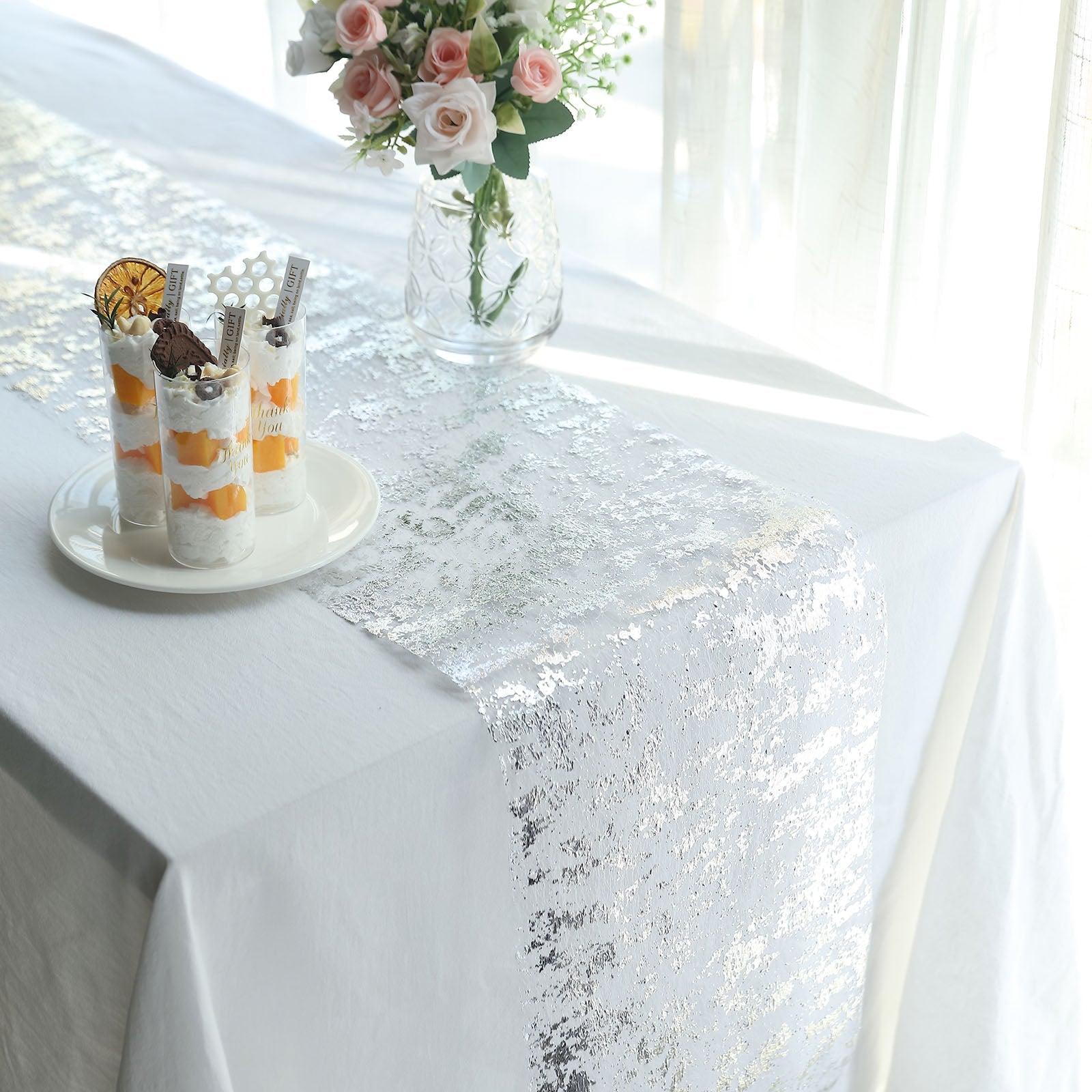 Sparkly metallic silver foil thin mesh table runner on a white table.