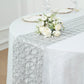 Metallic silver disposable table runner on a white tablecloth with floral decor.