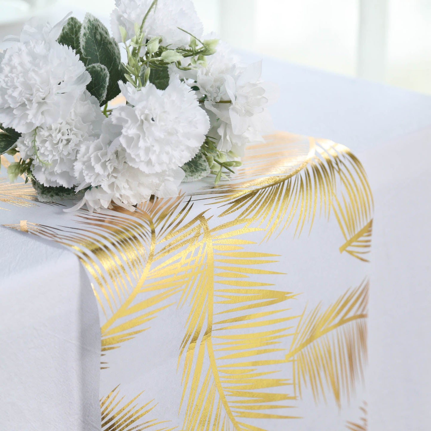 Metallic gold foil palm leaves table runner on white tablecloth.