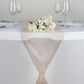 Peach sheer organza table runner on a white table with glassware and flowers.