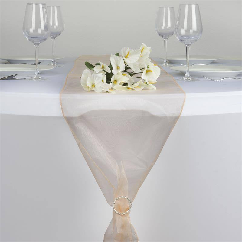 Peach sheer organza table runner on a white table with glassware and flowers.