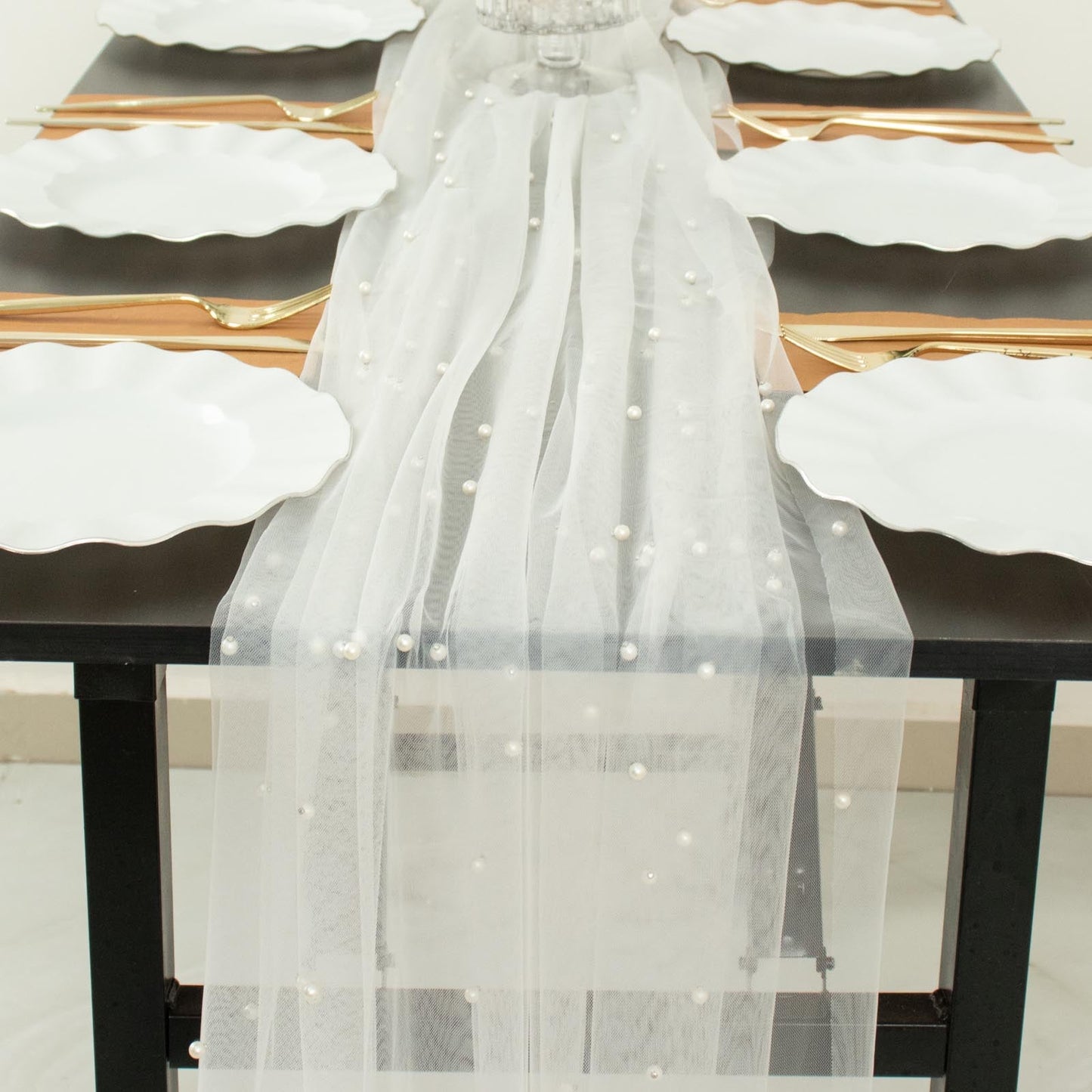 White pearl embellished sheer tulle table runner on a black table setting.