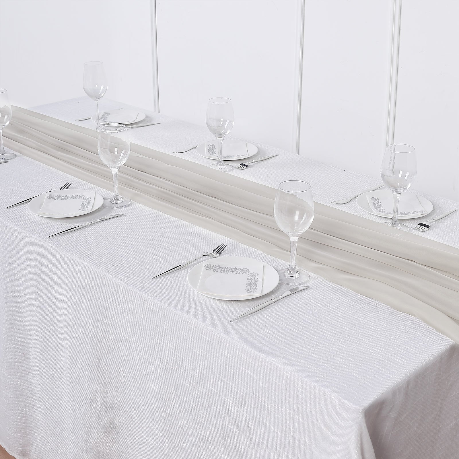 Beige chiffon table runner on a dining table setting with glasses and plates.