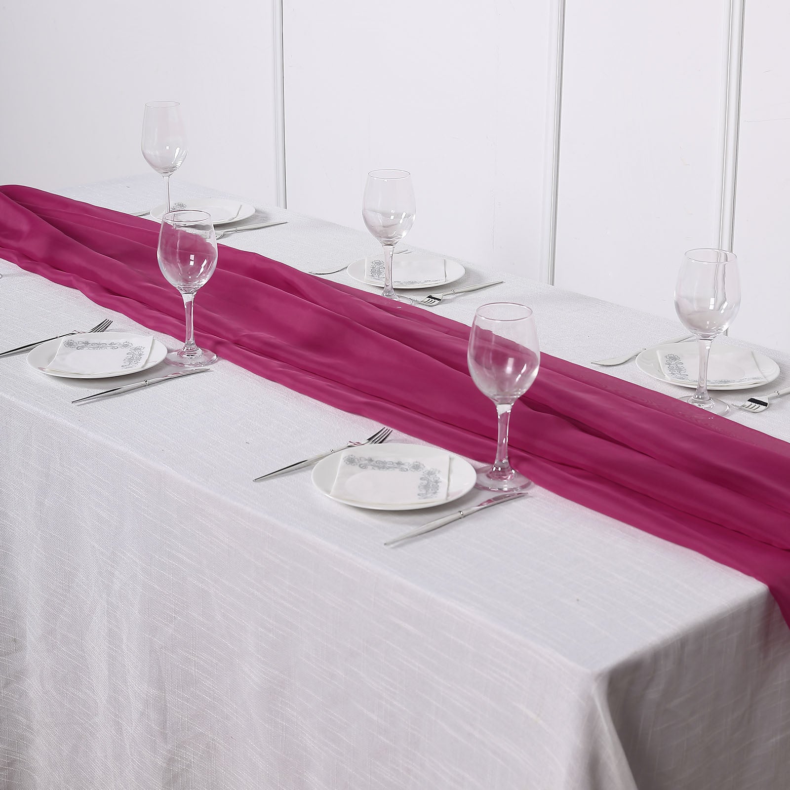 Fuchsia chiffon table runner on a white table setting.